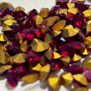 May include: A pile of red and gold rhinestones. The rhinestones are faceted and have a shiny finish.