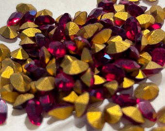 Puede incluir: Un montón de piedras de imitación rojas y doradas. Las piedras de imitación son facetadas y tienen un acabado brillante.