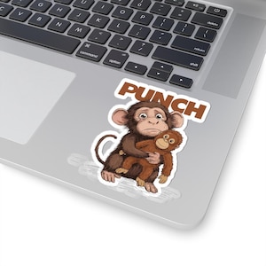 May include: A sticker featuring a cartoon monkey hugging a smaller monkey. The sticker has the word "PUNCH" in brown block letters above the monkeys. The monkeys are brown and have sad expressions. The sticker is on a laptop.