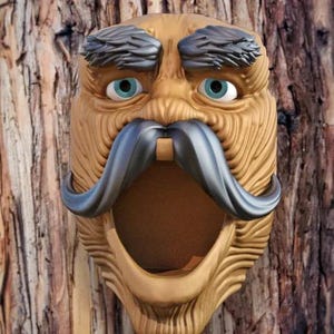 Puede incluir: Una talla de madera de una cara con una gran boca abierta, cejas espesas y un bigote grueso. La talla está pintada en tonos marrones y negros.