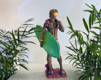 May include: A green surfboard with a pink base and a figurine of a person wearing yellow sunglasses and a purple towel. The figurine is standing on the base with one foot on the surfboard.