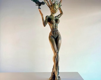 May include: A green and brown female figure sculpture with a tree-like head and a bird perched on her hand. The sculpture has a muscular physique and is standing on a tree trunk base.