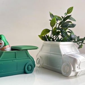 May include: Two miniature car-shaped planters, one green and one white. The green planter has a chocolate candy bar inside. The white planter has a small green plant growing inside.