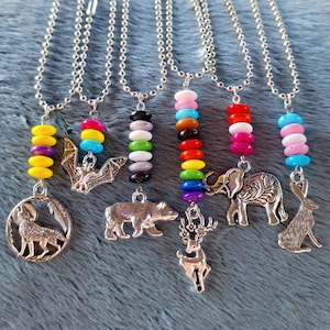 May include: Seven silver necklaces with different charms and colorful beads. The charms include a wolf, bat, bear, deer, elephant, and rabbit. The beads are arranged in a rainbow pattern.