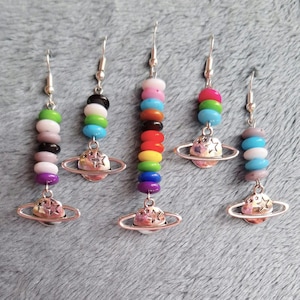May include: Five pairs of silver earrings with a planet charm and colorful beads. Each pair features a different color scheme of beads, including rainbow, black and white, gray and white, and blue and white.