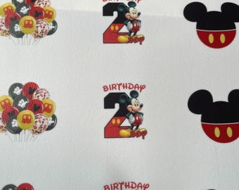 Op de afbeelding: Vier vellen wit papier met Mickey Mouse-thema verjaardagsparty decoraties. Elk vel heeft een rood nummer twee met Mickey Mouse er bovenop. Het nummer twee heeft witte stippen. De tekst "Birthday Boy" staat onder het nummer. Elk vel heeft ook een zwart Mickey Mouse-hoofd met rode oren en twee gele cirkels voor ogen. De vellen zijn versierd met een cluster van kleurrijke ballonnen met Mickey Mouse-ontwerpen.
