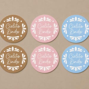 May include: Six circular stickers arranged in two rows of three. The stickers come in brown, pink, and light blue, each featuring a white decorative floral border and the text Cielito Lindo written in a white cursive script in the center.