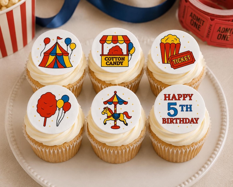 May include: Six cupcakes topped with white circular edible toppers featuring carnival-themed illustrations including a circus tent, cotton candy stand, popcorn, a ticket, a carousel horse, and text that reads Happy 5th Birthday in red and blue.