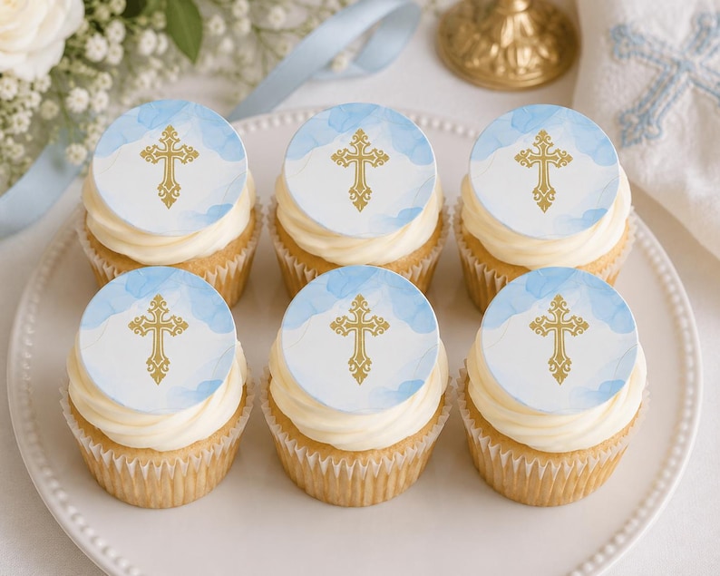 May include: Six cupcakes arranged on a white plate, each topped with a round edible topper featuring a gold cross design against a light blue watercolor background. The cupcakes have white frosting and are in white paper liners.