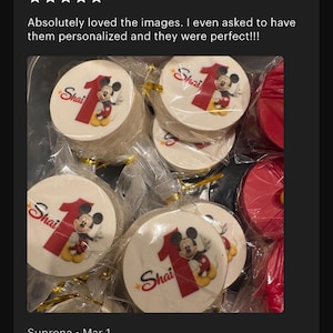 May include: Round white edible toppers individually wrapped in clear plastic, each featuring a red number one, the name Shai in red script, and a graphic of Mickey Mouse. The toppers are arranged in a group, with some red circular items visible.