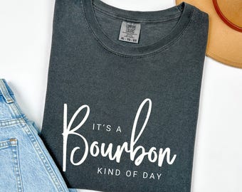 May include: A dark gray t-shirt with white text that reads "It's a Bourbon Kind of Day".