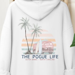 May include: White hooded sweatshirt with a graphic print of a red vintage van with surfboards, palm trees, and a sunset. The text "THE POGUE LIFE" is printed below the graphic, with the words "OUTER BANKS - NORTH CAROLINA" printed below that.