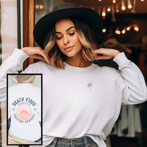 May include: White long-sleeved sweatshirt with a palm tree graphic on the front and "Beach Vibes Forever Chasing Sunsets" text with a sun and palm tree graphic on the back.