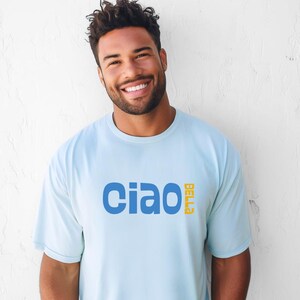 May include: Light blue t-shirt with the word "ciao" in blue and the word "bella" in yellow. The shirt is a solid color and has a crew neck.