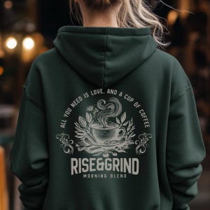 May include: Dark green hoodie with the text "ALL YOU NEED IS LOVE, AND A CUP OF COFFEE" and "RISE&GRIND MORNING BLEND" in white. The design features a coffee cup with steam, surrounded by leaves and cinnamon sticks.