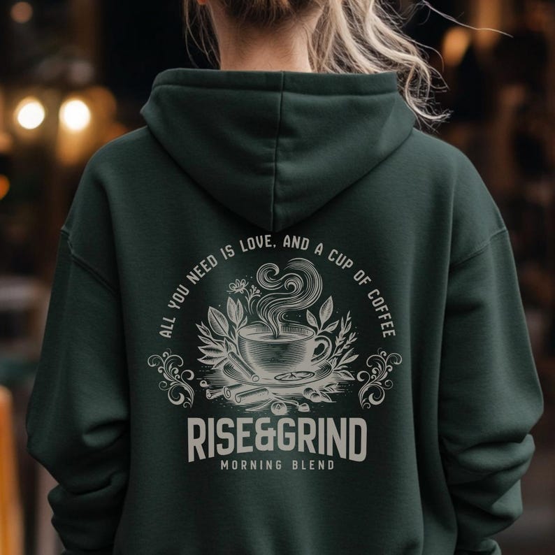 May include: Dark green hoodie with the text "ALL YOU NEED IS LOVE, AND A CUP OF COFFEE" and "RISE&GRIND MORNING BLEND" in white. The design features a coffee cup with steam, surrounded by leaves and cinnamon sticks.