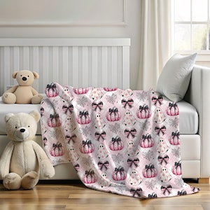 May include: Pink and black Halloween themed throw blanket with a repeating pattern of ghosts, pumpkins, and bows.