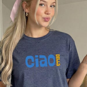 May include: Navy blue t-shirt with the word "Ciao" in blue and "Bella" in yellow. The shirt is made of a soft material.