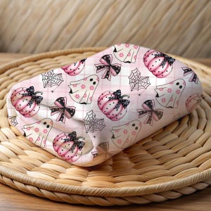 May include: Pink and white fabric with a repeating pattern of ghosts, pumpkins, bows, and spiderwebs. The fabric has a plaid background.