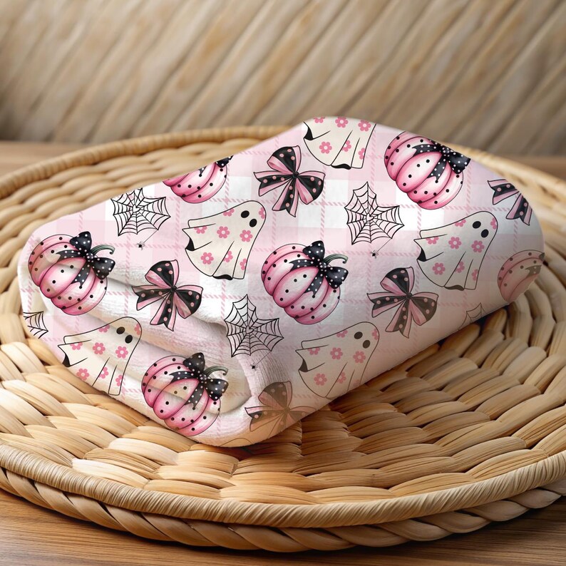 May include: Pink and white fabric with a repeating pattern of ghosts, pumpkins, bows, and spiderwebs. The fabric has a plaid background.