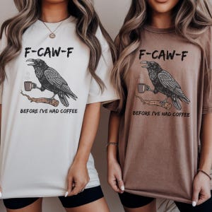 May include: Two t-shirts, one cream and one brown, featuring a raven graphic holding a coffee cup on a branch. The text "F-CAW-F" and "BEFORE I'VE HAD COFFEE" are printed above and below the raven illustration.