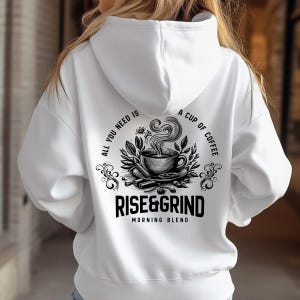 May include: White hoodie with a black and white graphic on the back. The graphic features a coffee cup with steam, surrounded by leaves and cinnamon sticks, and the text "ALL YOU NEED IS A CUP OF COFFEE" and "RISE&GRIND MORNING BLEND".