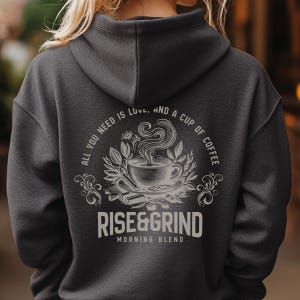 May include: Dark gray hoodie with a coffee-themed graphic on the back. The design includes a coffee cup, steam, and the text "ALL YOU NEED IS LOVE, AND A CUP OF COFFEE" and "RISE&GRIND MORNING BLEND".