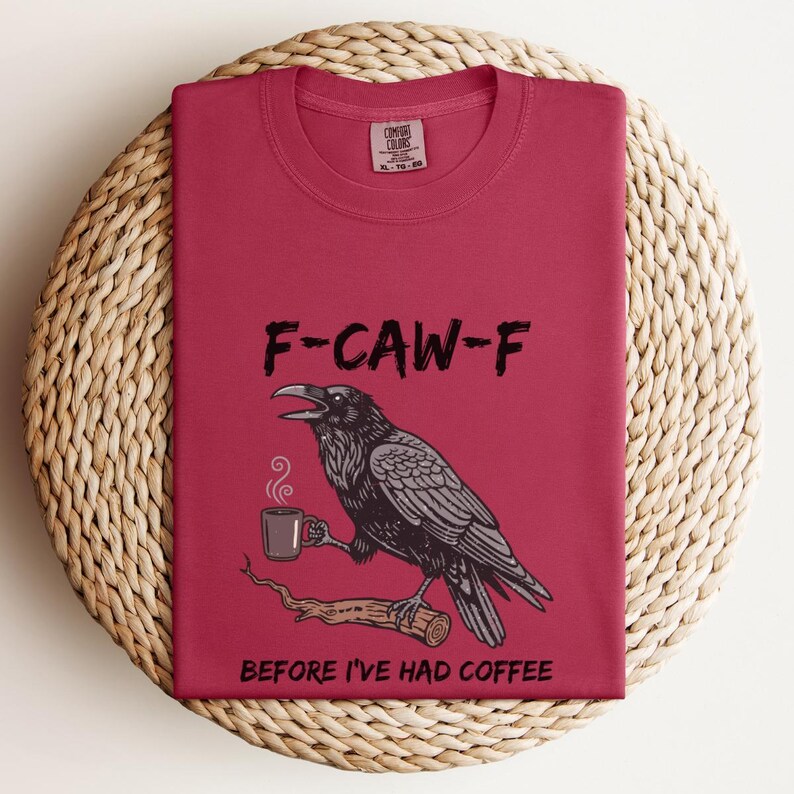May include: A maroon t-shirt with the text "F-CAW-F" above a black and gray illustration of a raven holding a coffee cup. The text "BEFORE I'VE HAD COFFEE" is below the raven.