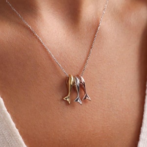 Könnte beinhalten: Eine silberne Kettenkette mit einem Anhänger aus drei kleinen Fisch-Anhängern. Die Fische sind in Gold, Silber und Roségold.