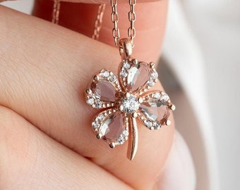 Puede incluir: Un collar de oro rosa con un colgante de trébol de cuatro hojas con piedras preciosas transparentes y rosadas.