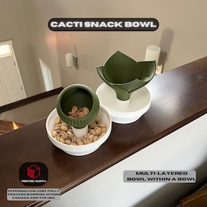 Könnte beinhalten: Eine grüne, kaktusförmige Snackschale mit weißem Sockel. Die Schale ist mit Pistazien gefüllt. Die Schale ist ein mehrschichtiges Design mit einer kleineren Schale in einer größeren Schale. Der Text "CACTI SNACK BOWL" ist über der Schale gedruckt. Der Text "PRINT3D NORTH" ist unter der Schale gedruckt. Der Text "OFFERING LOW COST, FULLY TRACKED SHIPPING WITHIN CANADA AND THE USA" ist unter dem Logo gedruckt.