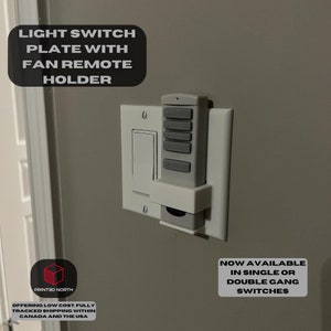 May include: A white light switch plate with a holder for a fan remote. The remote is gray and has five buttons. The text "NOW AVAILABLE IN SINGLE OR DOUBLE GANG SWITCHES" is printed on a white rectangle below the switch plate.