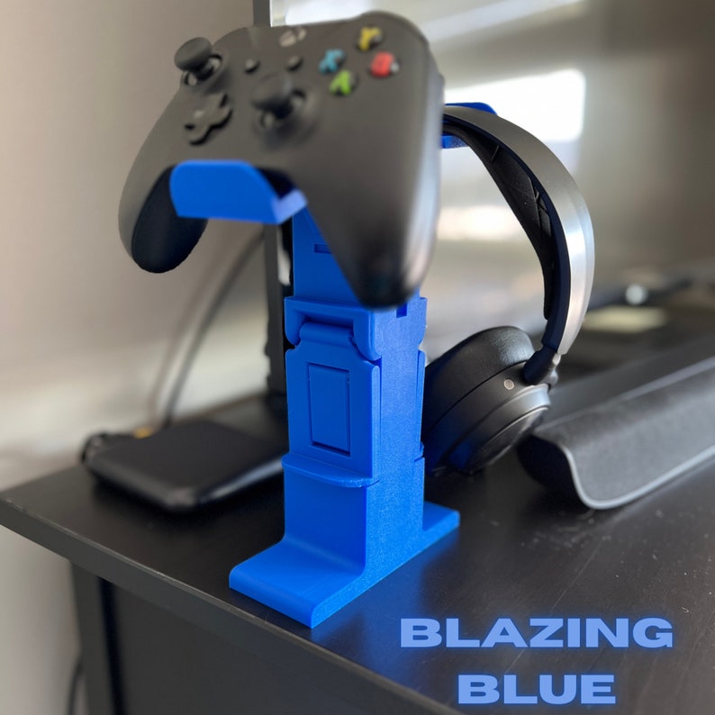 May include: A blue 3D printed stand for a gaming headset and controller. The stand has a slot for the headset and a hook for the controller. The stand is labelled "BLAZING BLUE".