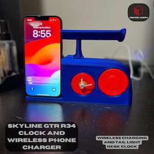 Puede incluir: Un reloj de escritorio impreso en 3D azul y rojo con un cargador de teléfono inalámbrico y una luz trasera. El reloj tiene forma de coche y tiene una pantalla digital de la hora. El cargador de teléfono está en el lateral del reloj y la luz trasera en la parte posterior. El texto "SKYLINE GTR R34 CLOCK AND WIRELESS PHONE CHARGER" está impreso en la parte delantera del reloj. El texto "WIRELESS CHARGING AND TAIL LIGHT DESK CLOCK" está impreso en la parte posterior del reloj.