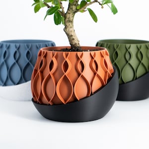 May include: Three decorative planters in blue, orange, and green, each with a wave-like pattern. The orange planter holds a small bonsai tree. Each planter sits on a black, curved base. The planters are designed for indoor use.