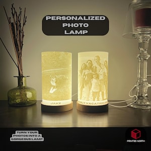 May include: Two personalised photo lamps with wooden bases. The lamp on the left has a photo of a dog named Jake. The lamp on the right has a photo of a family on holiday. The text "Personalized Photo Lamp" is at the top of the image. The text "Turn your photos into a gorgeous lamp" is at the bottom of the image.