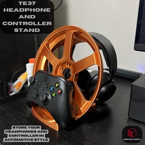 Könnte beinhalten: Ein orangefarbener Kopfhörer- und Controller-Ständer in Form eines Autorads. Ein schwarzer Controller liegt auf dem Ständer, mit einem schwarzen Kopfhörer in der Mitte des Rades. Der Ständer trägt den Text "TE37 HEADPHONE AND CONTROLLER STAND".