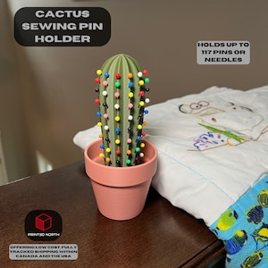 May include: A green cactus-shaped sewing pin holder with a terracotta pot. The cactus is filled with colourful sewing pins. The text "HOLDS UP TO 117 PINS OR NEEDLES" is visible in the image.
