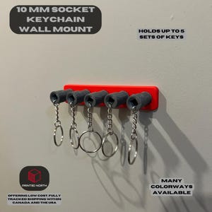 May include: A red wall-mounted keychain holder with five grey 10 mm socket keychains. The holder is labelled "10 MM SOCKET KEYCHAIN WALL MOUNT" and "HOLDS UP TO 5 SETS OF KEYS".