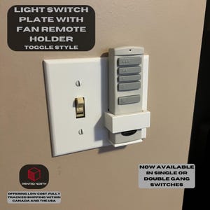 May include: White light switch plate with a holder for a fan remote. The remote is white with gray buttons and the text "NOW AVAILABLE IN SINGLE OR DOUBLE GANG SWITCHES".