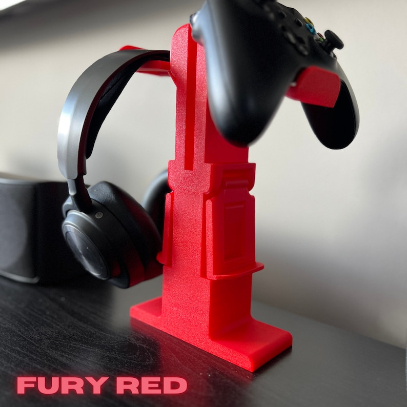 May include: A red plastic stand for holding a gaming headset and controller. The stand is designed to hold the headset on the side and the controller on top. The stand is labelled "FURY RED".
