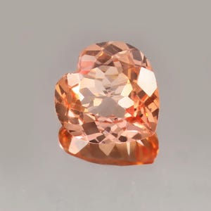 以下が含まれることがあります： 桃色のハート型の宝石。 宝石には光を反射する多くのファセットがあり、キラキラとした効果を生み出しています。 ハート型の宝石はニュートラルな背景に配置されています。