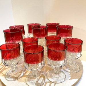 May include: Set of 12 ruby red glass goblets with clear glass stems and bases. The goblets have a textured, diamond-like pattern.