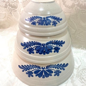 May include: Set of three white ceramic bowls with blue floral designs. The bowls are stacked on top of each other, with the largest bowl on the bottom and the smallest bowl on top.