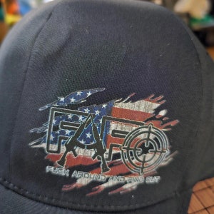 May include: A black baseball cap with a distressed American flag design and the text "F.A.F.O.  F**uck Around And Find Out" printed on the front.