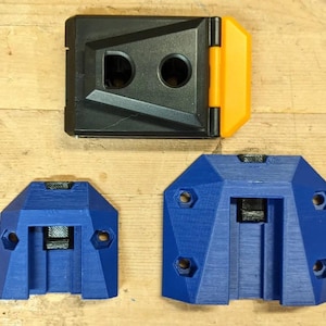 May include: Three 3D printed wall mounts, one black with a yellow hinge, and two blue. The blue mounts have hexagonal screw holes and a slot for a rail.