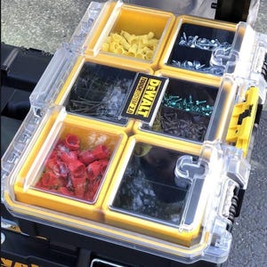 May include: A yellow and black DeWalt ToughSystem 2.0 toolbox with six clear compartments. The compartments are filled with various hardware, including screws, nuts, bolts, and wire connectors. The compartments are labelled with the DeWalt logo and the ToughSystem 2.0 name.