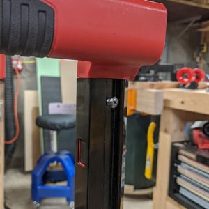May include: Close-up of a red and black metal handle with a silver screw. The handle is attached to a black metal pole.