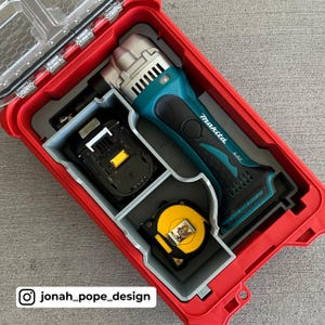May include: A red tool box with a grey insert. The insert has compartments for a teal and black Makita oscillating tool, a battery, and a yellow tape measure.