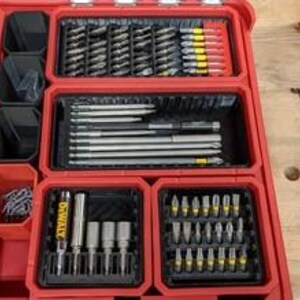 May include: A red toolbox with multiple compartments filled with various types of drill bits, screws, and other tools. The toolbox is organised with different sized compartments to hold different types of tools.